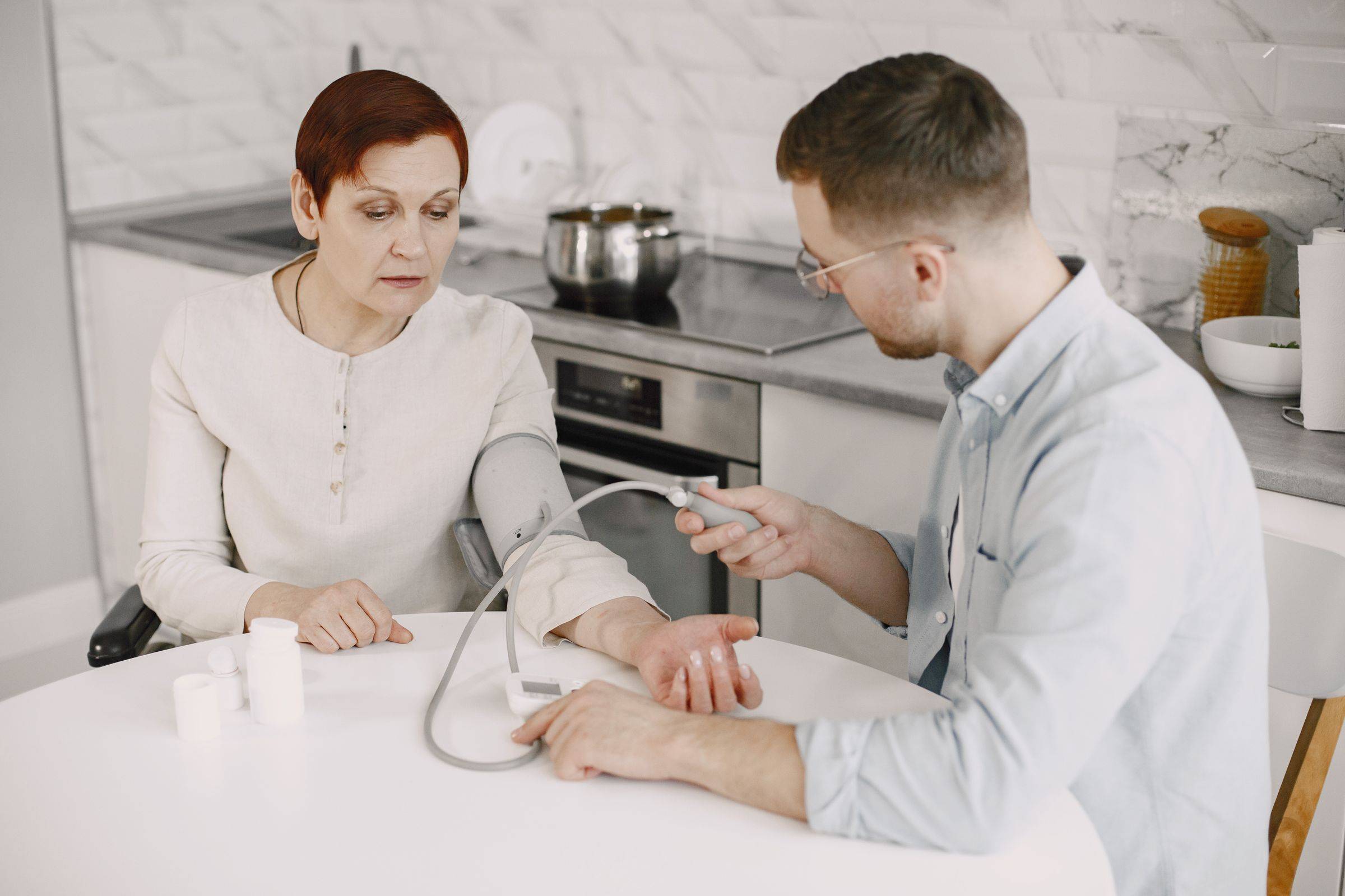 A clinician takes an older woman’s blood pressure at her kitchen table.